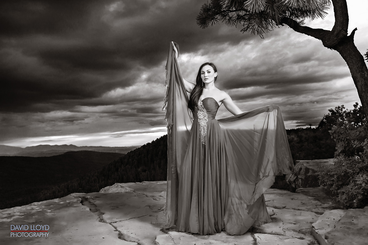 black and white woman standing on edge of cliff in dark dress, high fashioned photography, glamour photography