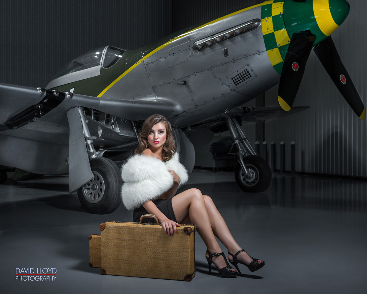 woman wearing a green dress and white fur top sitting on luggage cases in front of old military plane, photography in atlanta, old school photography, classic photography, model photography, glamour photography, photography workshop 