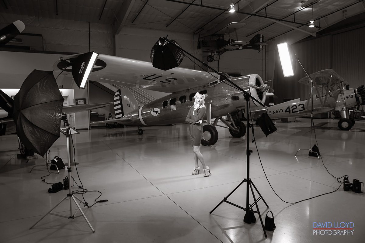 woman standing in front of old military plane in large hanger with photography lighting around her, photography workshop, photography, david lloyd photography, 